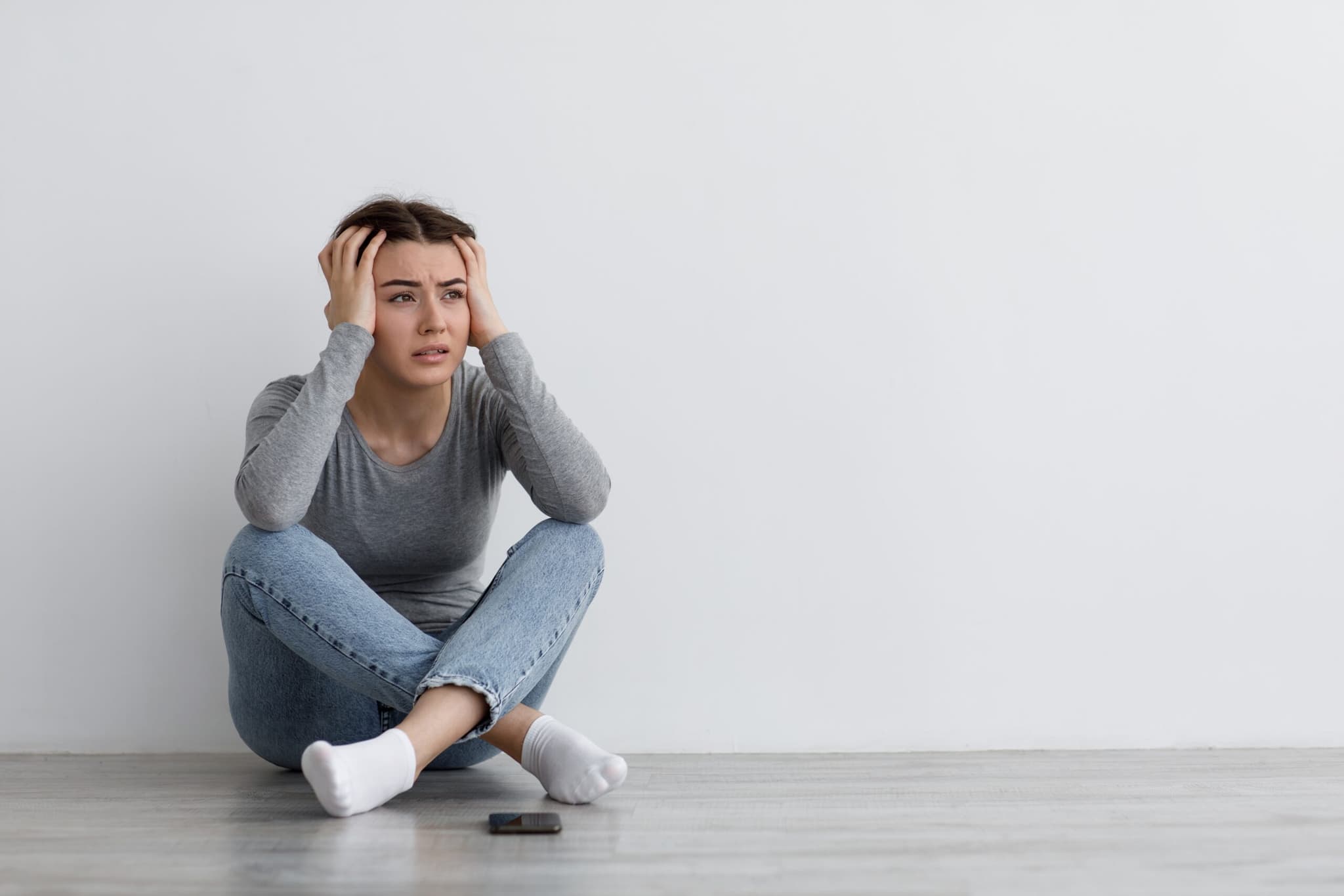 Woman sitting on the floor with her knees drawn up and both hands on her head.