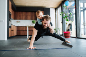 father,working,out,,doing,single,arm,plank,with,his,jolly